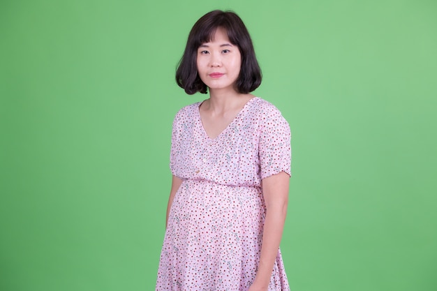 Portrait of beautiful Asian pregnant woman with short hair against chroma key or green wall