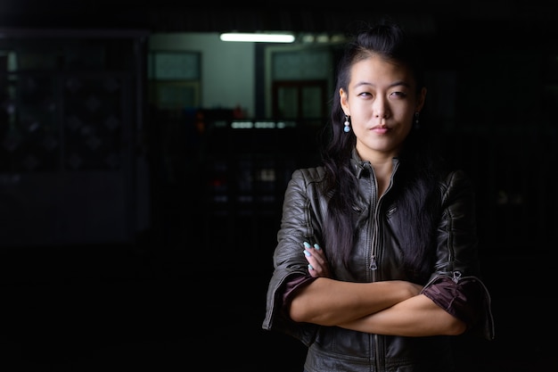 Portrait of beautiful Asian rebellious woman wearing leather jacket in the streets outdoors at night