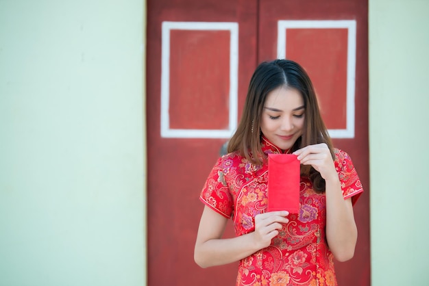 チャイナドレスの美しいアジアの女性の肖像タイの人々幸せな中国の旧正月のコンセプト赤い封筒を持って赤