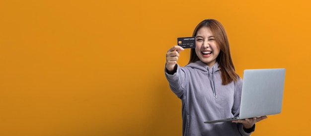 Portrait of beautiful Asian woman holding credit card and laptop on isolated background portrait concept used for advertisement and signage isolated over yellow background copy space