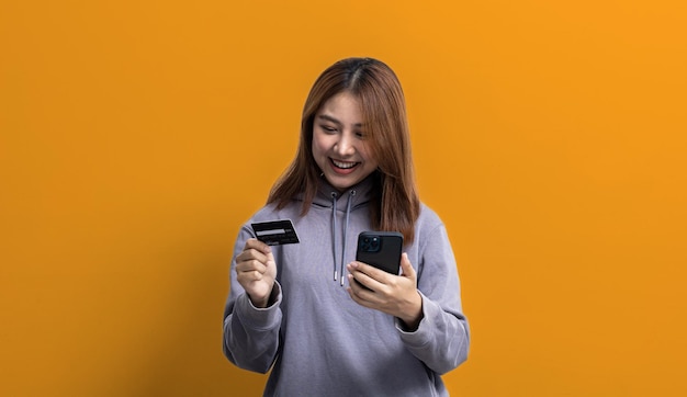 노란색 배경 복사 공간에 격리된 광고 및 간판에 사용되는 격리된 배경 초상화 개념에 신용카드와 휴대전화를 들고 있는 아름다운 아시아 여성의 초상화