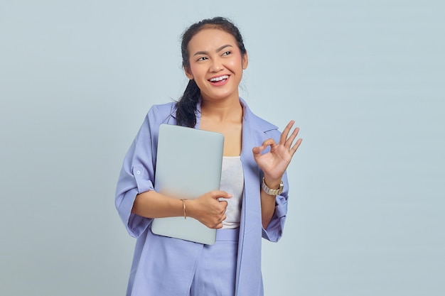 Portrait of beautiful Asian woman holding laptop smiling and showing ok sign over white background