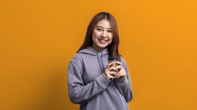 Portrait of beautiful Asian woman holding a paper coffee cup on isolated yellow background portrait concept used for advertisement and signage isolated over blue background copy space