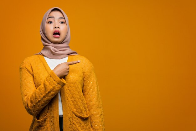 Portrait of beautiful Asian woman shocked and pointing to empty space