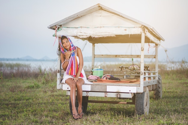 Portrait of beautiful Asian woman sitting on mini tractor at countryside of Thailand with  lake and 