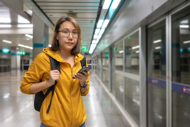 Portrait beautiful asian woman standing holding a smartphone waiting for the subway