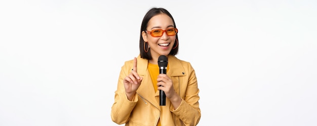 Portrait of beautiful asian woman in sunglasses stylish girl singing giving speech with microphone holding mic and smiling standing over white background