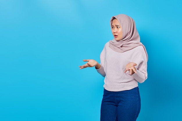 Portrait of beautiful asian woman surprised with confused and displeased expression on blue background