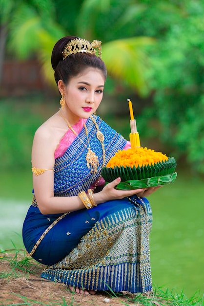Портрет красивой азиатской женщины в традиционном тайском платье, молящейся держать кратонг для участия в фестивале лой кратонг в таиланде