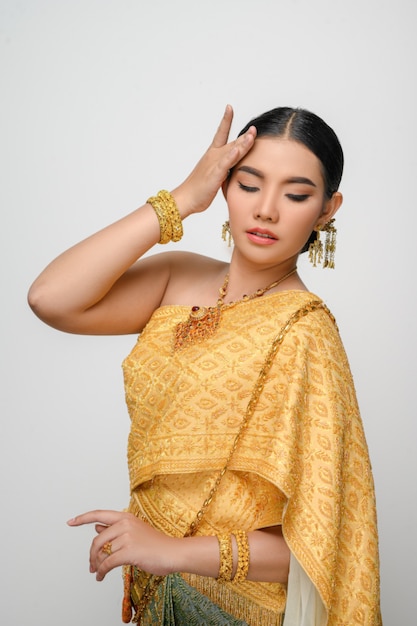 Portrait beautiful Asian woman in traditional Thai dress costume smile and pose hand on her forhead with gracefully on white wall