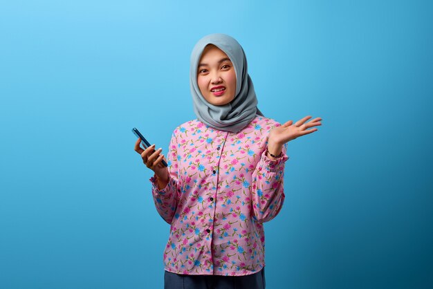 青い背景に混乱した表情で携帯電話を使用して美しいアジアの女性の肖像画