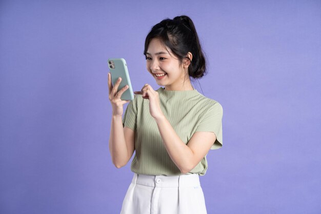 紫色の背景にスマートフォンを使用する美しいアジアの女性の肖像画