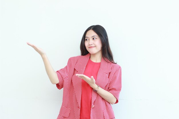 Portrait of beautiful asian woman wearing red outfit pointing to the side for copy space with smiling gesture isolated on white background