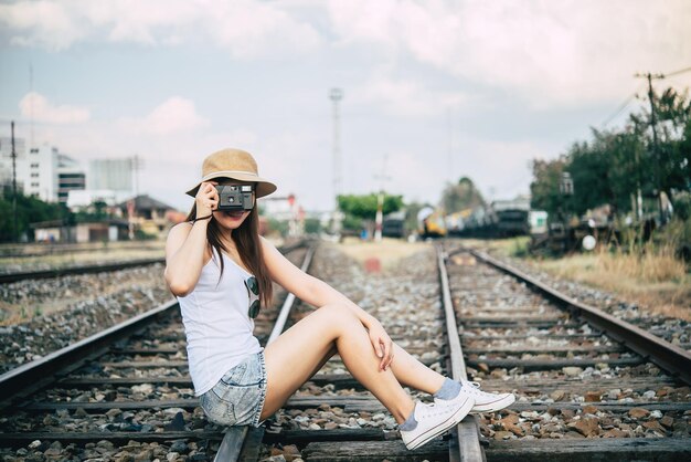 Портрет красивой азиатской женщины в белой футболке с фотоаппаратом в руке на железной дороге в винтажном стиле