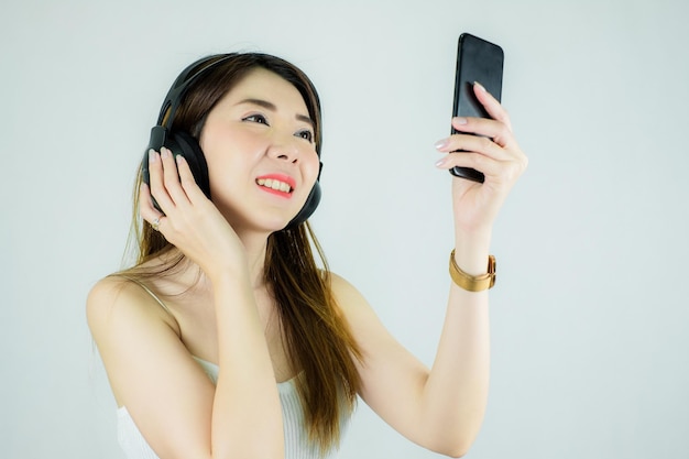 Foto ritratto di bella donna asiatica con cuffie e dispositivo mobile che ascolta la musica. modello femminile felice, sorridente/caucasico isolato su priorità bassa bianca.