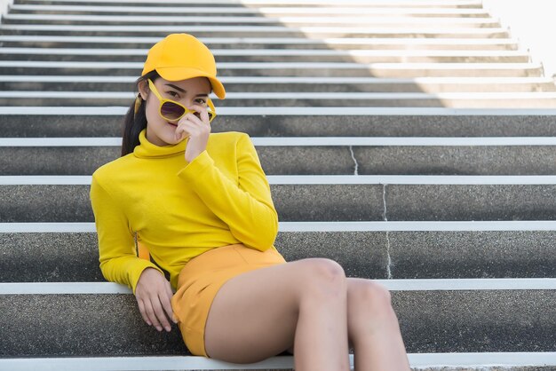 Portrait of beautiful asian woman in yellow clothsHipsters girl wear yellow hat sit on stair for take a pictureThailand people