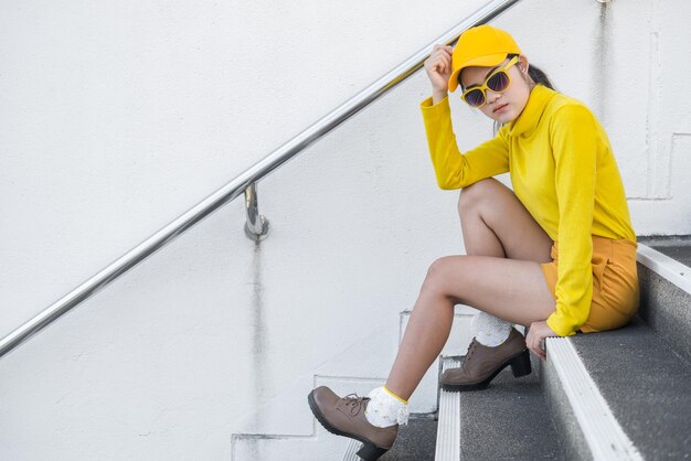 Portrait of beautiful asian woman in yellow clothshipsters girl\
wear yellow hat on stair for take a picturethailand people in\
yellow tone style