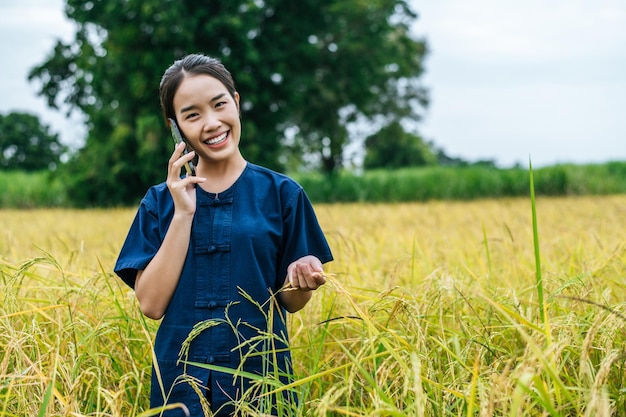 Ritratto di una bella giovane agricoltrice asiatica usa lo smartphone in un campo di riso biologico e sorride con felicità