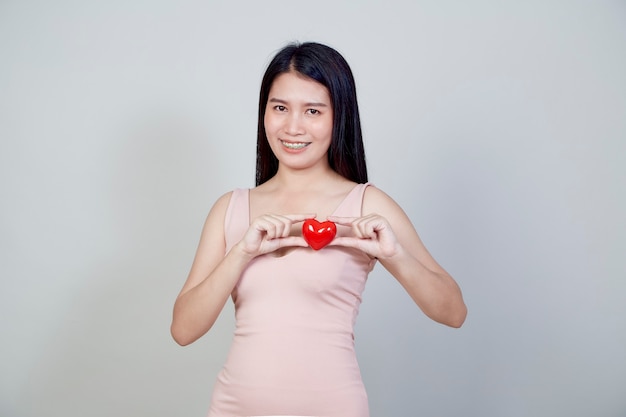 Portrait of beautiful Asian young woman holding pointing red heart shape isolated on light gray background with copy space