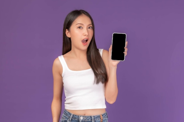 Ritratto di bella giovane donna asiatica che mostra smartphone con schermo nero schermo vuoto copia spazio vuoto per banner pubblicitario isolato su sfondo viola mock up image