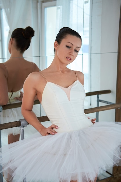 Portrait of beautiful ballerina in tutu leaning on barre and looking down.