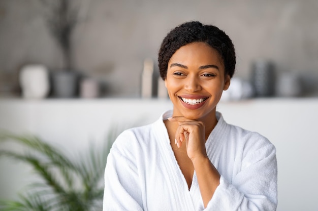 Portrait of beautiful black woman in white bathrobe touching chin and smiling