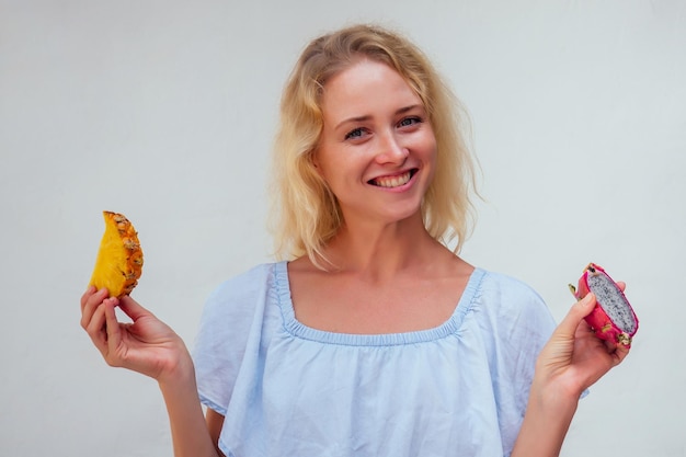 Portrait of beautiful blond hair woman with blue eyes holding pineapple and dragon fruit on white backgrounddetox and allergy to tropical products