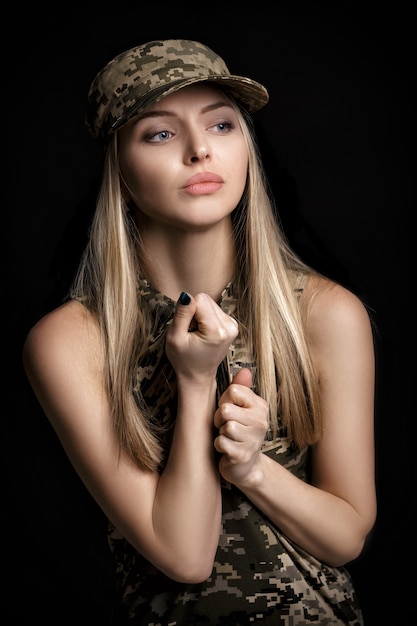 Portrait of a beautiful blond woman soldiers in military attire on black background