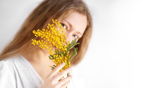 미모사의 노란 꽃을 손에 들고 하얀 드레스를 입은 아름다운 금발 여성의 초상화