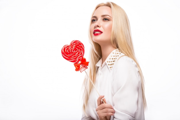 Portrait of beautiful blond woman with bright makeup and red candy heart in hand