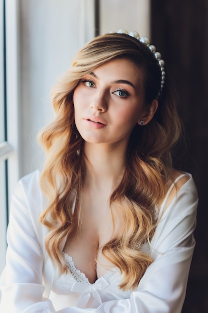 Portrait of a beautiful blonde bride in the interior. Morning young bride in a bathrobe. Wedding photography. Smiling and cute girl stands.