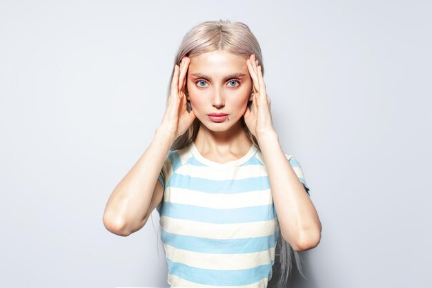 Portrait of beautiful blonde girl holding hands on temples on white background