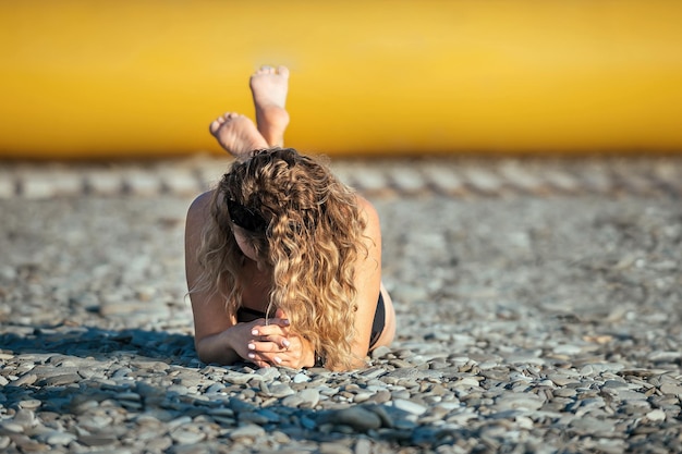 Portrait of a beautiful blonde girl with wavy long hair, she lies in a swimsuit on the beach