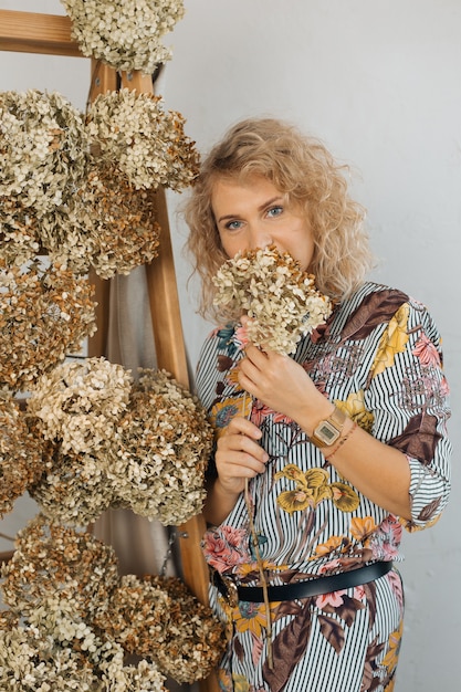 Portrait of beautiful blonde woman, flowers in her face, interior decorator florist, smiling looking into frame. copy space. natural fall decor concept.