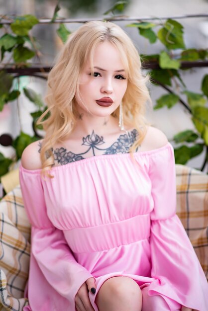 Portrait of a beautiful blonde woman with burgundy lips in a pink sexy dress posing on the balcony
