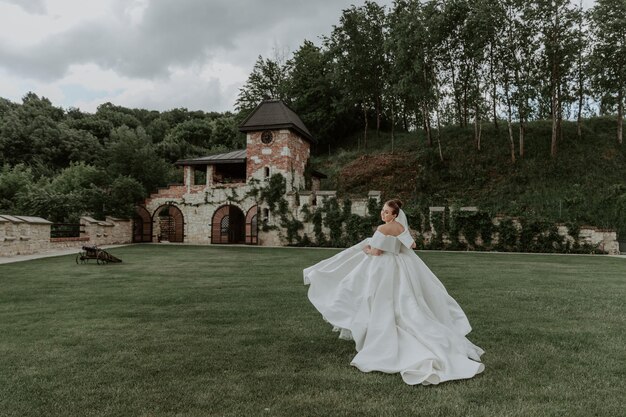 Portrait of beautiful bride in beige wedding dress with modern curly hairstyle and veil walking on g