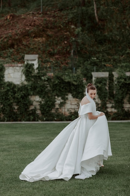 Portrait of beautiful bride in beige wedding dress with modern curly hairstyle and veil walking on g