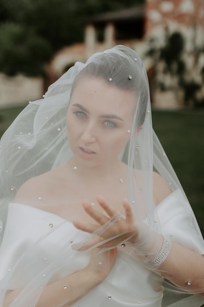 Portrait of beautiful bride in beige wedding dress with modern curly hairstyle and veil walking on g