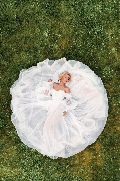 Portrait of a beautiful bride lying on the ground in a white wedding dress