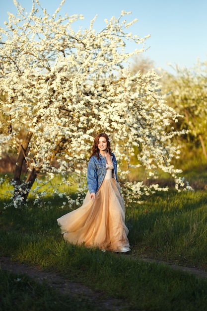 Portrait of a beautiful bride. Wedding concept. Stylish wedding. Great sunset light. She is wearing a blue denim jacket, dress. Spring blooming garden.