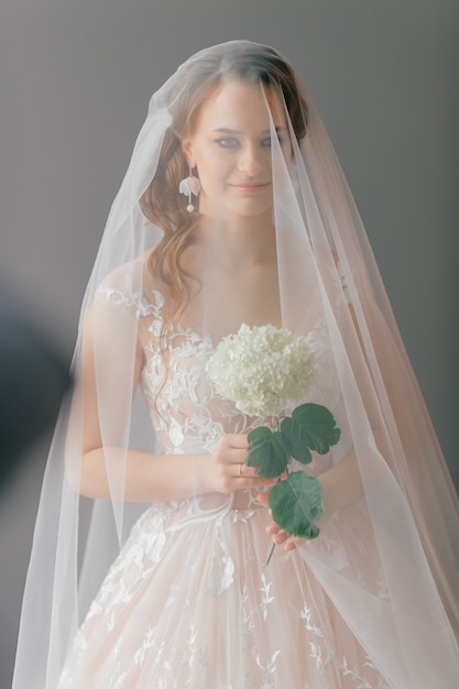 Portrait of beautiful bride in white vintage dress with flower in her hands posing under veil