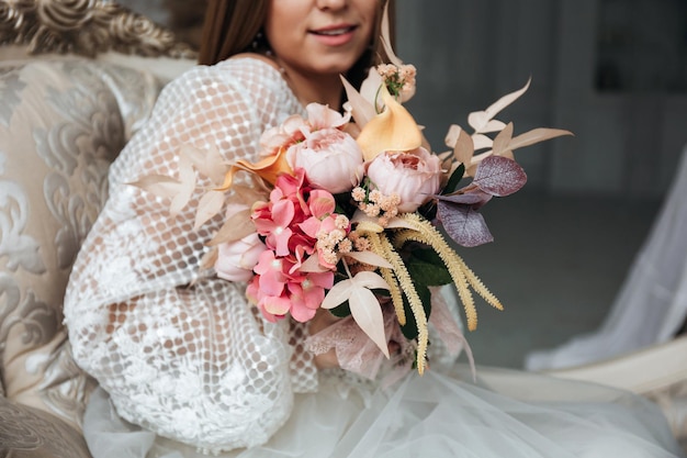 Portrait of a beautiful bride with a bouquet of hydrangea roses and feces in pastel orange color in her hands in a light interior