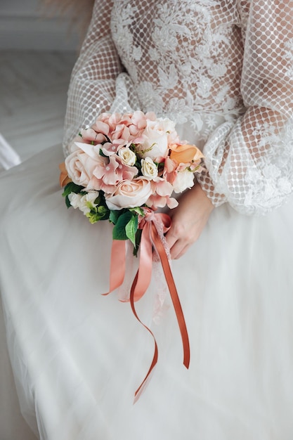 Foto ritratto di una bella sposa con un bouquet di ortensie arancio pastello e rose in mano in un interno chiaro