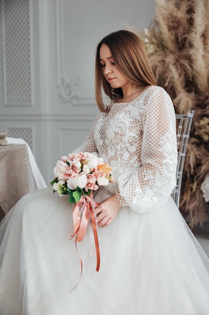 Foto ritratto di una bella sposa con un bouquet di ortensie arancio pastello e rose in mano in un interno chiaro