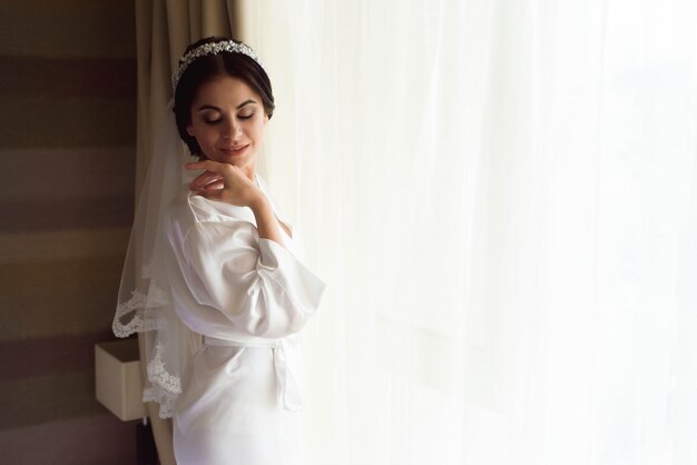 Портрет красивой невесты с вуалью моды представляя на кровати на утре свадьбы. Составить. Брюнетка Свадебная фата.