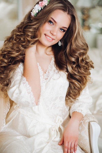 Portrait of beautiful bride with long hair in white lingerie looking at the camera, smiling.