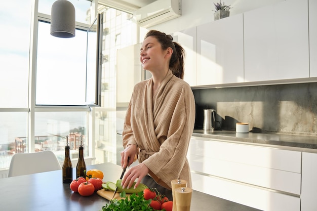 portrait of beautiful brunette girl chopping vegetables for meal making salad in the kitchen eating