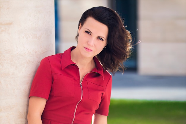 Portrait of beautiful brunette girl, young pretty woman in red dress  outdoors at summer day. Sexy serious attractive female model, tricky lady.