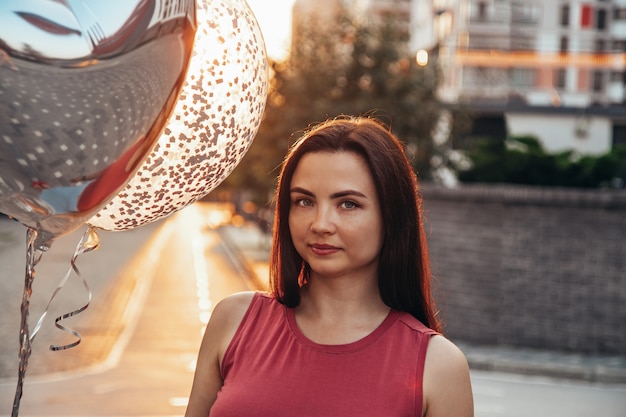 Ritratto di una bella bruna con palloncini al tramonto in città.