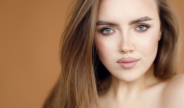 Portrait of a beautiful brunette with clear skin and expressive eyes on a brown background